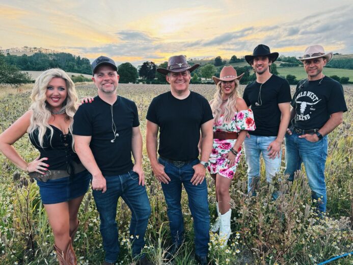 The Wild Ones Country Band standing in a countryside field at sunset in western-style outfits