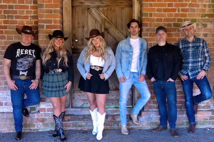 he Wild Ones Country Band posing in western-style outfits in front of a rustic brick barn door