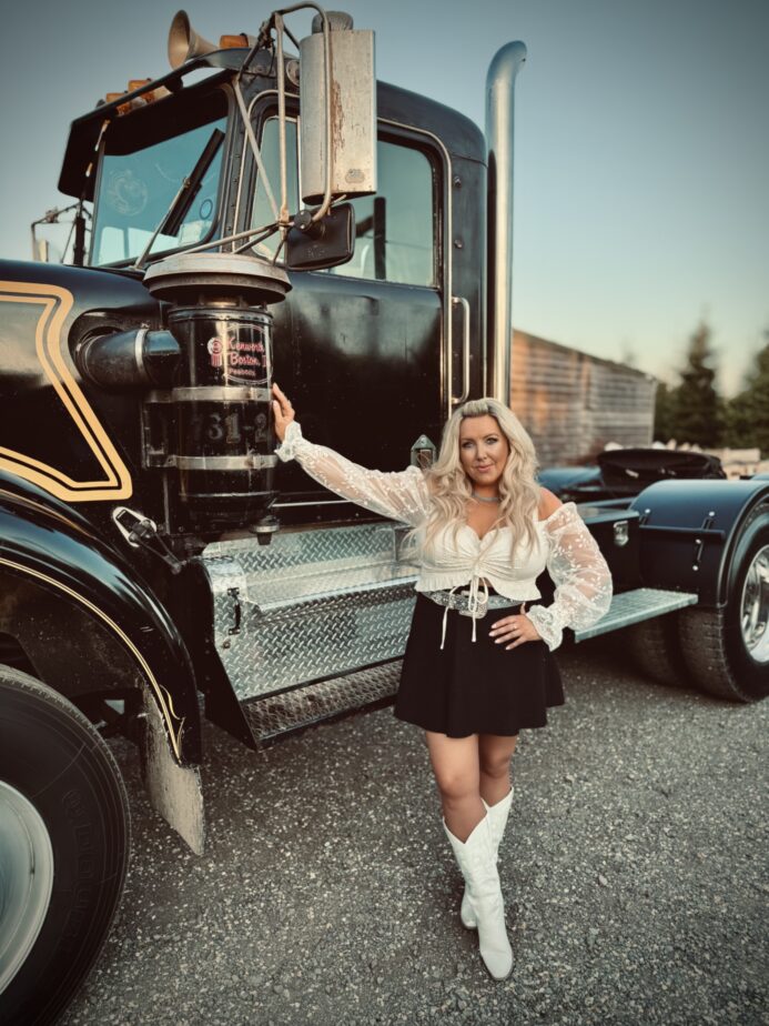Female vocalist from The Wild Ones Country Band posing beside a classic black truck in western-style outfit
