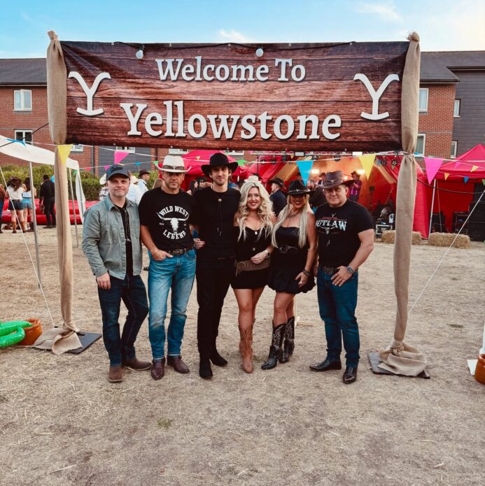 The Wild Ones Country Band posing under a Yellowstone-style sign at a UK western-themed event